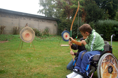 Das Ziel im Visier: Ein Schüler sitzt in seinem Rollstuhl, spannt mit Unterstützung einen Bogen und nimmt eine Zielscheibe in den Blick.